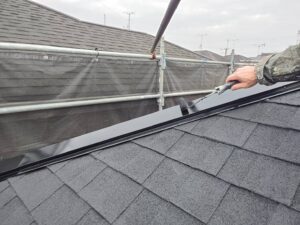 新居浜市で屋根棟包みの金属部分を上塗り塗装している様子